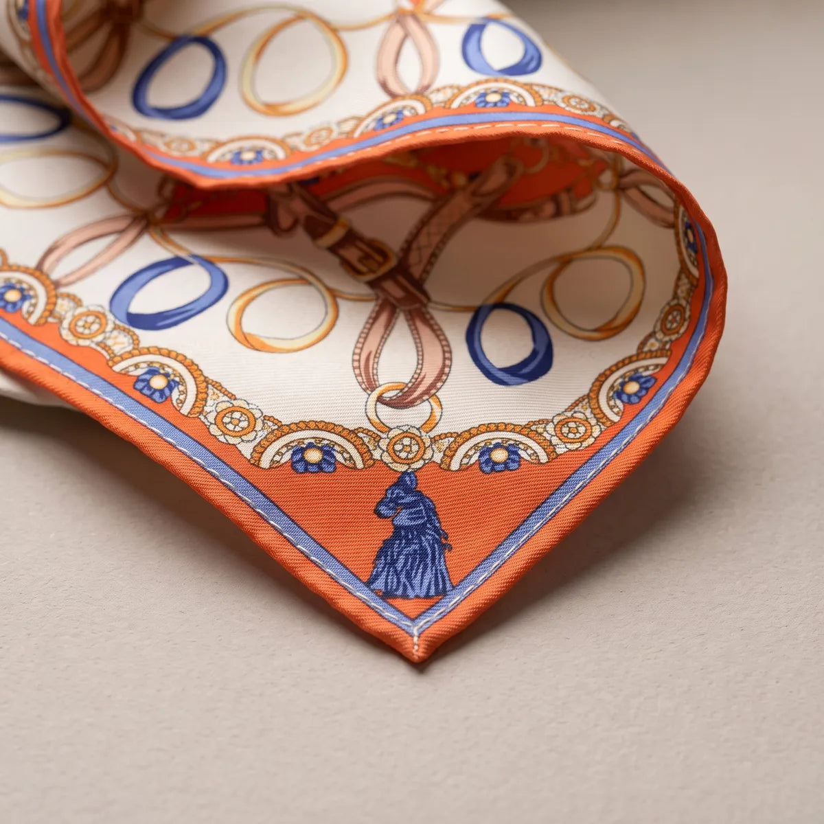 Corner of the orange shawl: a blue horse-head tassel on orange, the beaded border and a periwinkle line along the edge