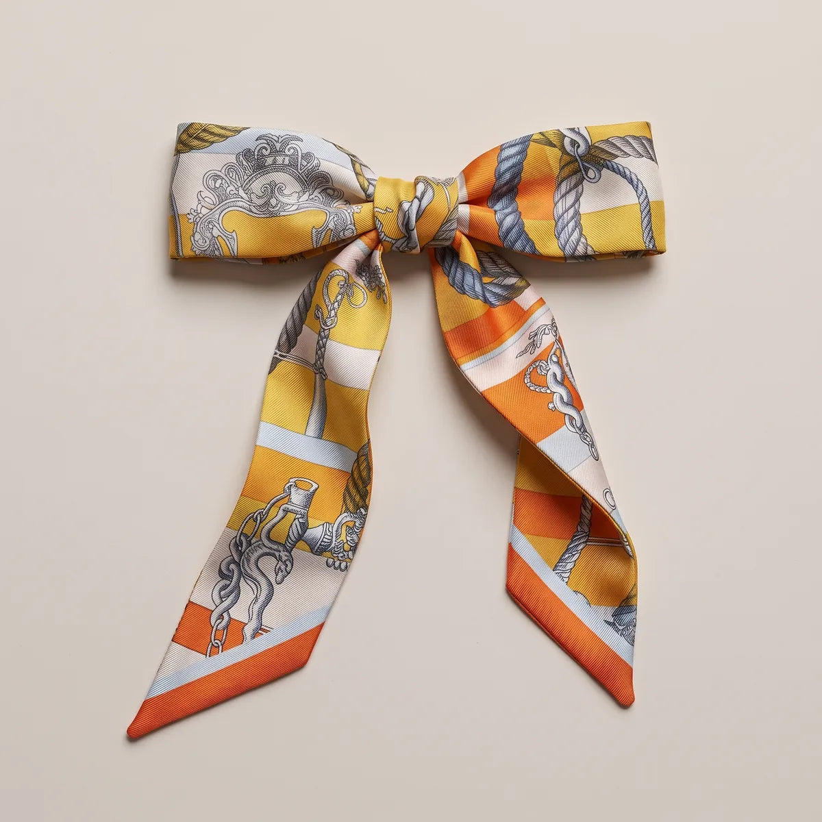 Orange and yellow skinny silk scarf tied in a bow, a crest and twisted rope on the loops