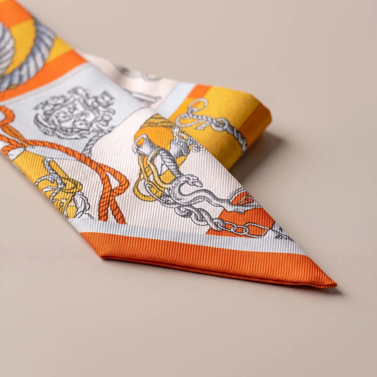 Orange tip of the skinny scarf folded over: a heraldic crest, an orange cord and a gray chain