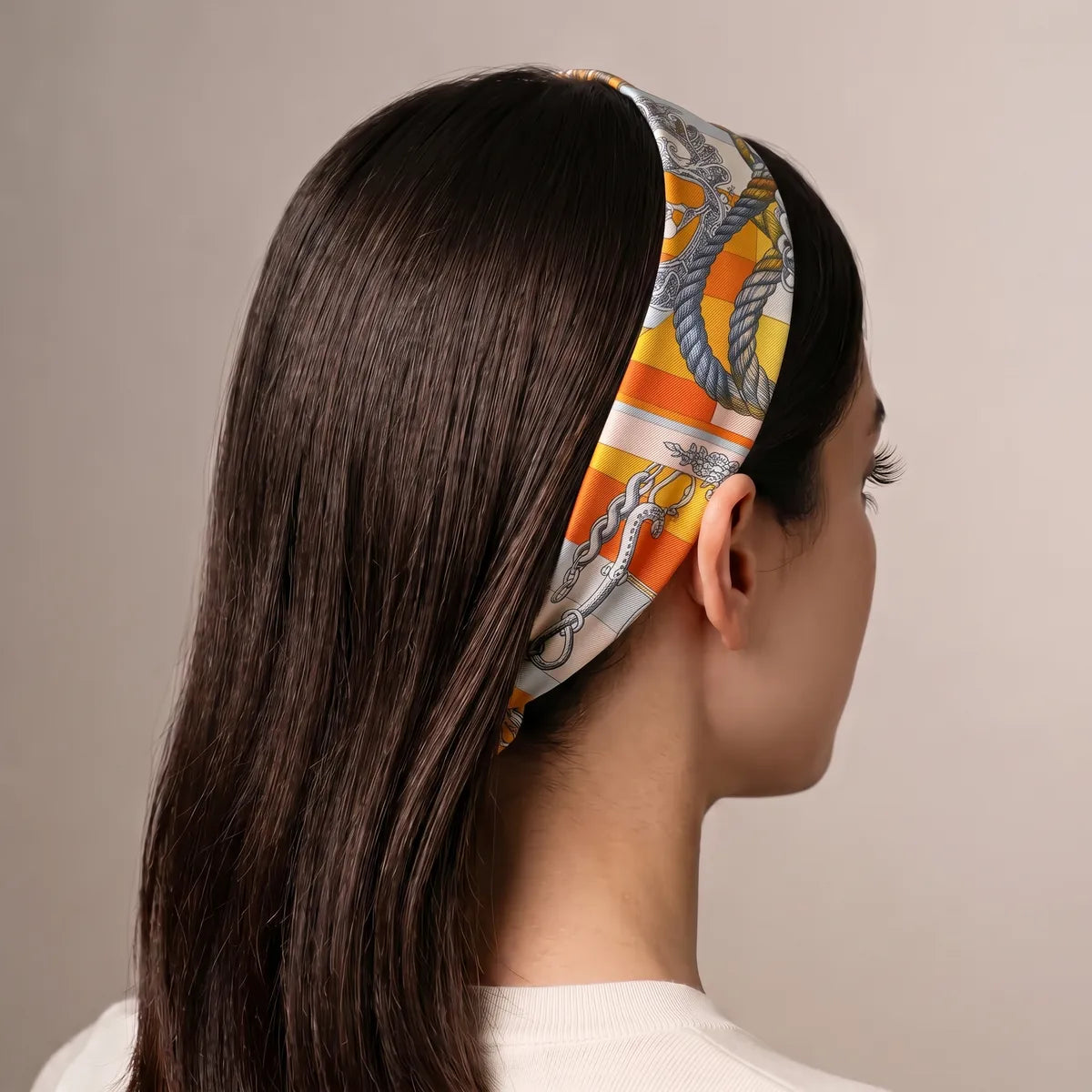Orange chain print skinny scarf worn as a headband over long dark hair