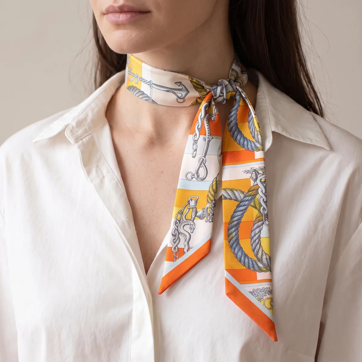 Orange chain print skinny scarf knotted at the neck, small anchor near the collar