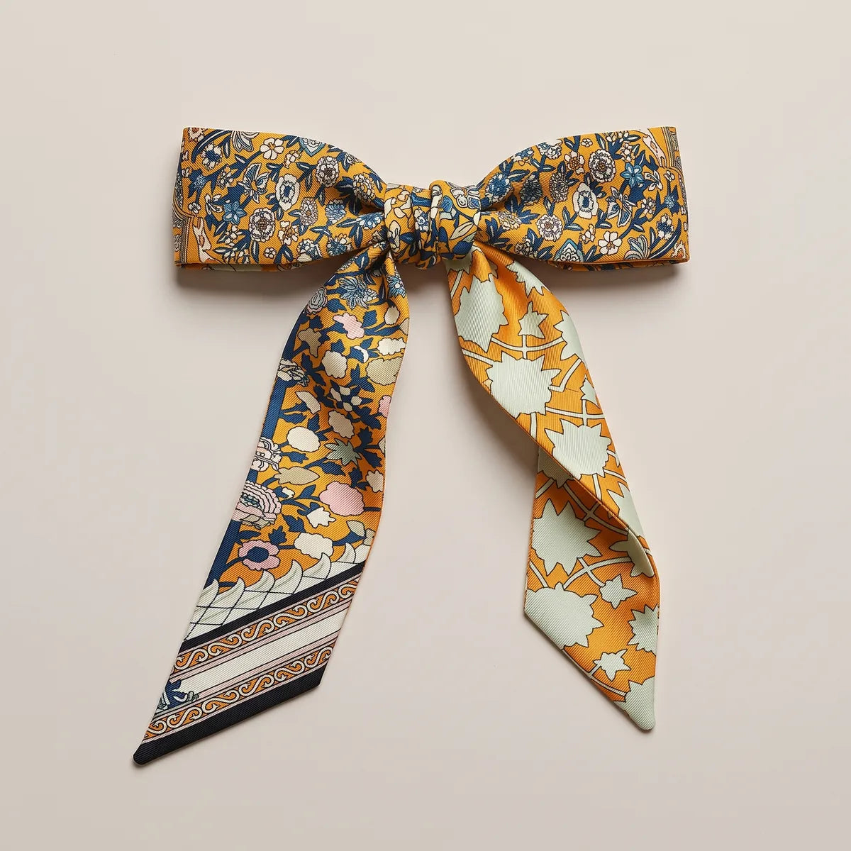 Orange skinny silk scarf tied in a flat bow, navy flowers on the loops and mint stars on one tail