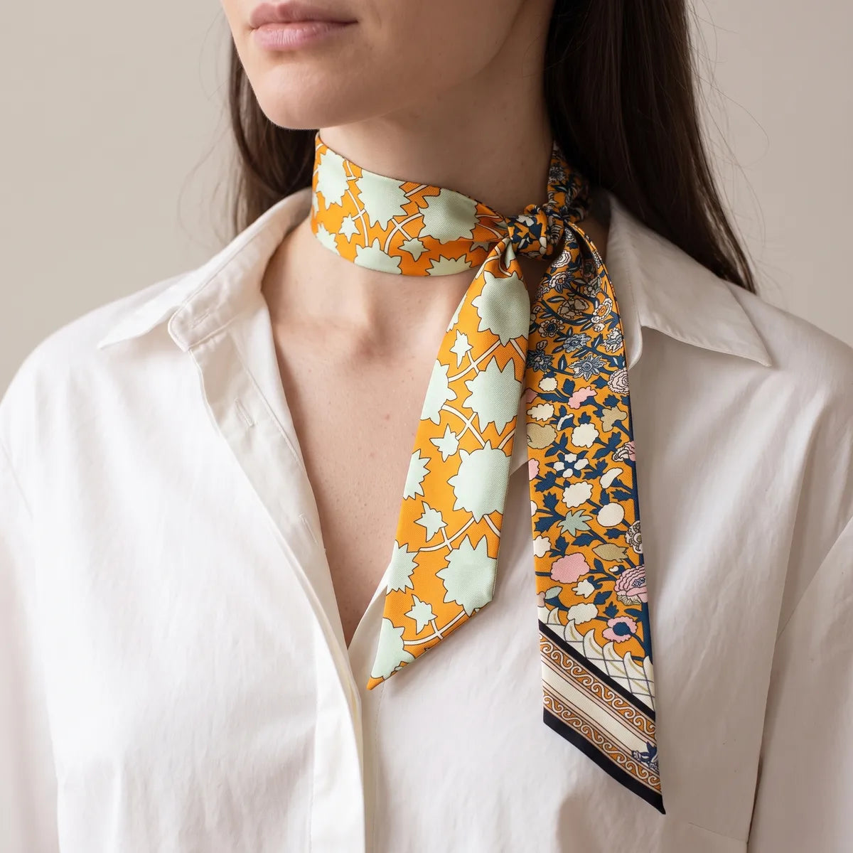 Woman in a white shirt wearing the orange floral skinny scarf knotted at the side of her neck