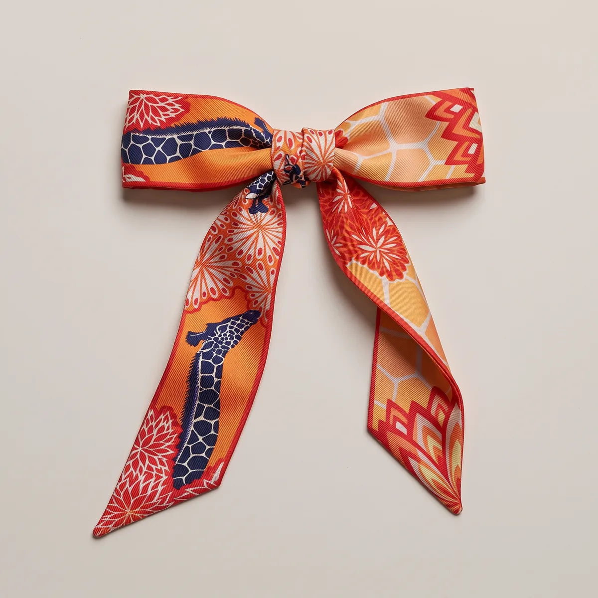 Orange skinny silk scarf tied into a flat bow, a navy giraffe on one tail and red flowers above