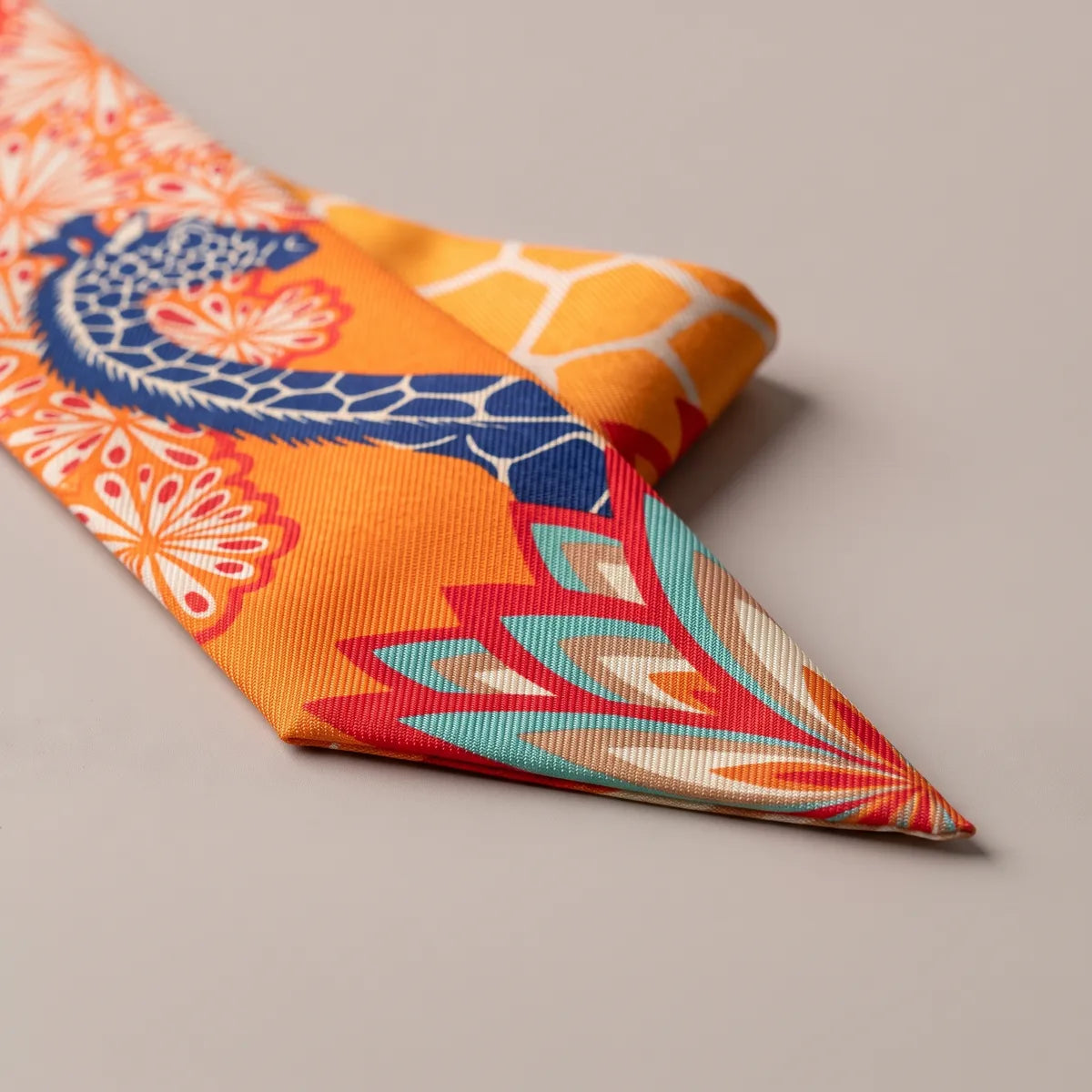 Close-up of the orange skinny scarf: a giraffe's neck and a fan of red and turquoise petals at the tip