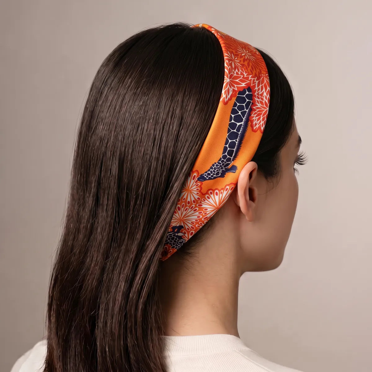 Orange giraffe skinny scarf worn as a headband on long dark hair, seen from behind