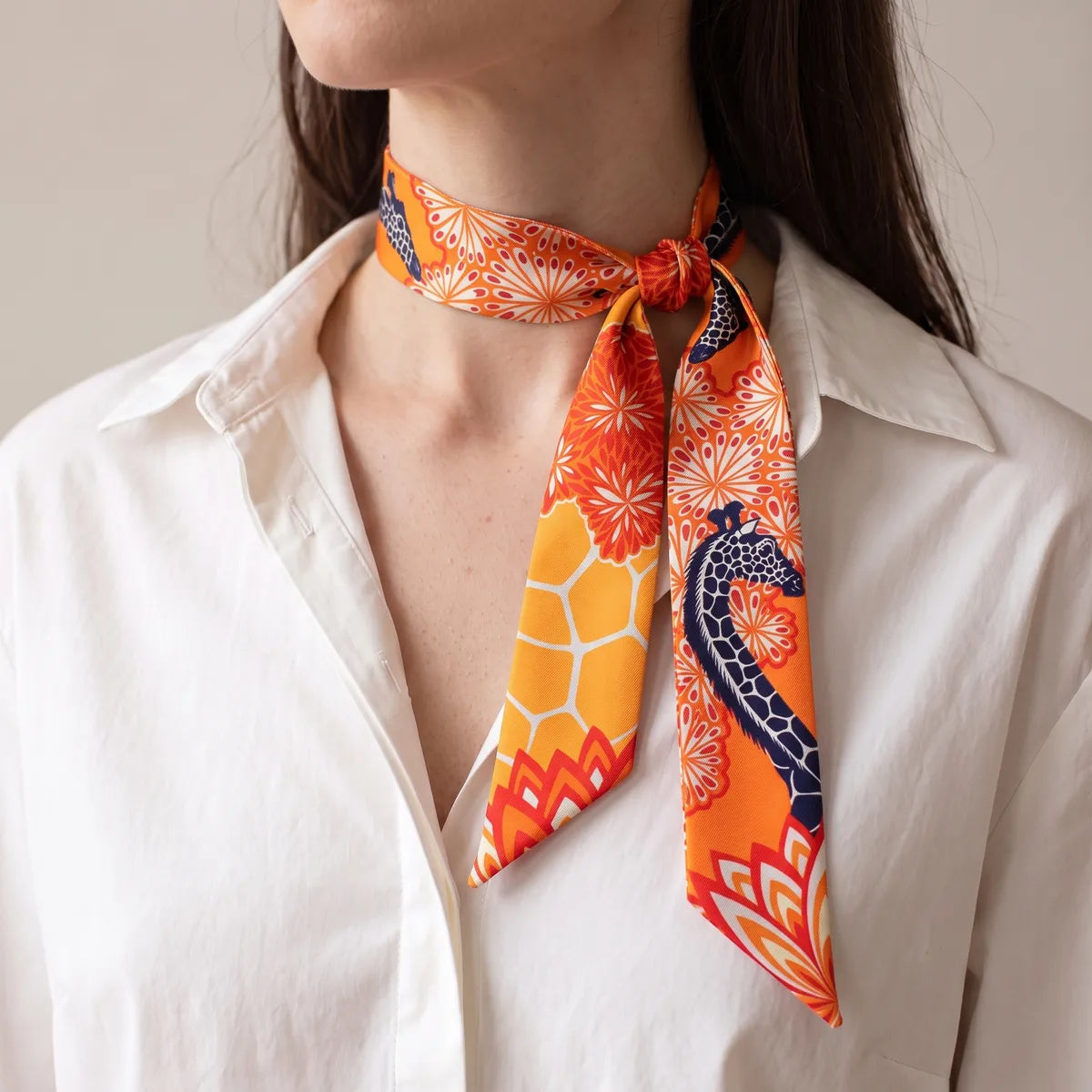 Woman in a white shirt wearing the orange giraffe skinny scarf knotted at the side of her neck