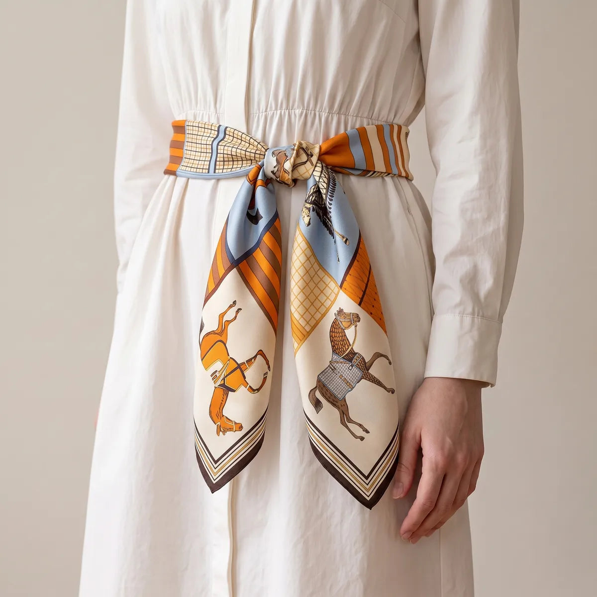 Horse print silk square tied as a belt at the waist of a white shirt dress, two corners hanging