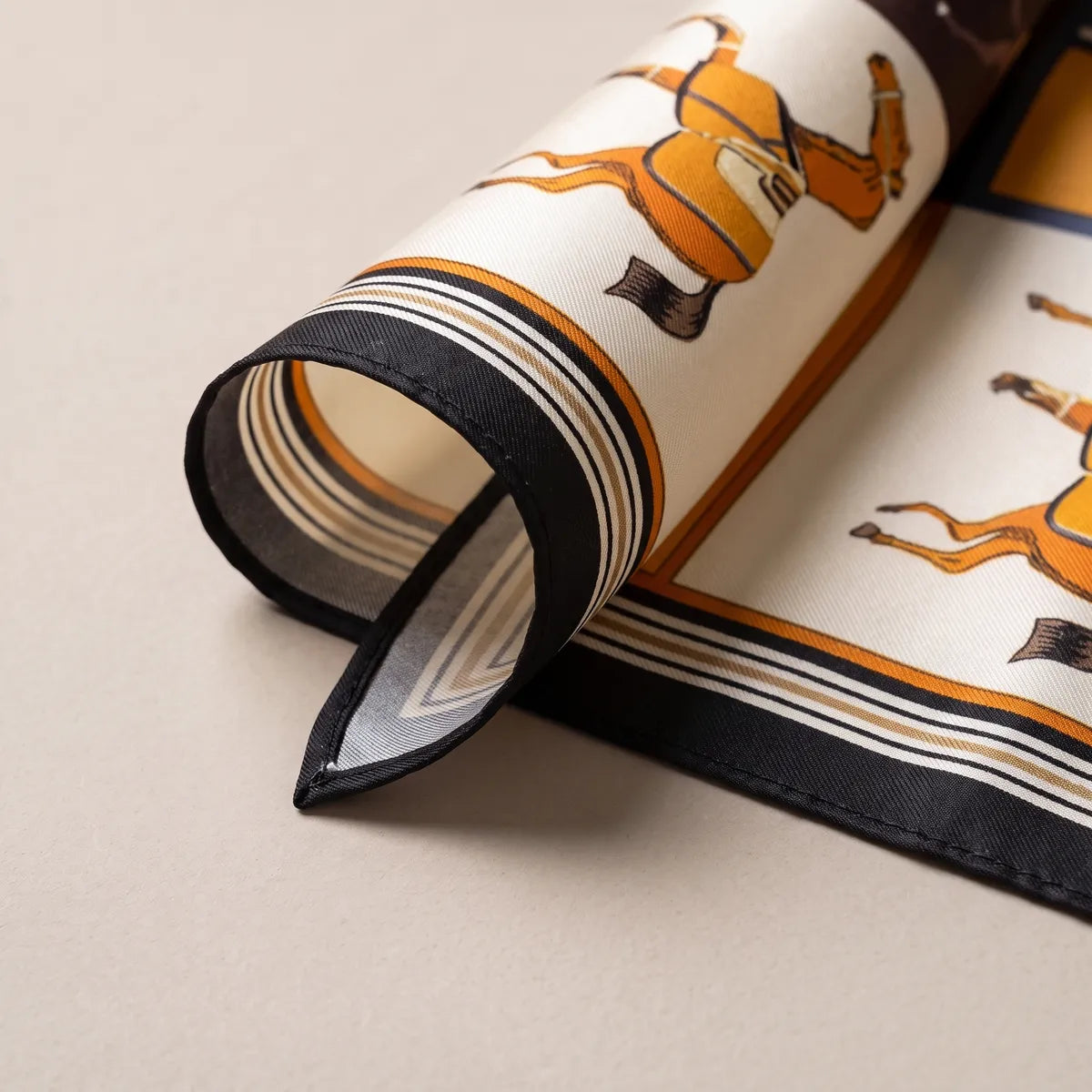 Corner of the orange horse scarf rolled back to show the black edge, striped frame and paler reverse
