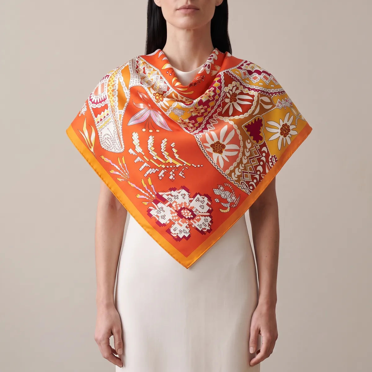 Woman in a cream dress wearing the orange patchwork silk shawl over her shoulders, point at the front