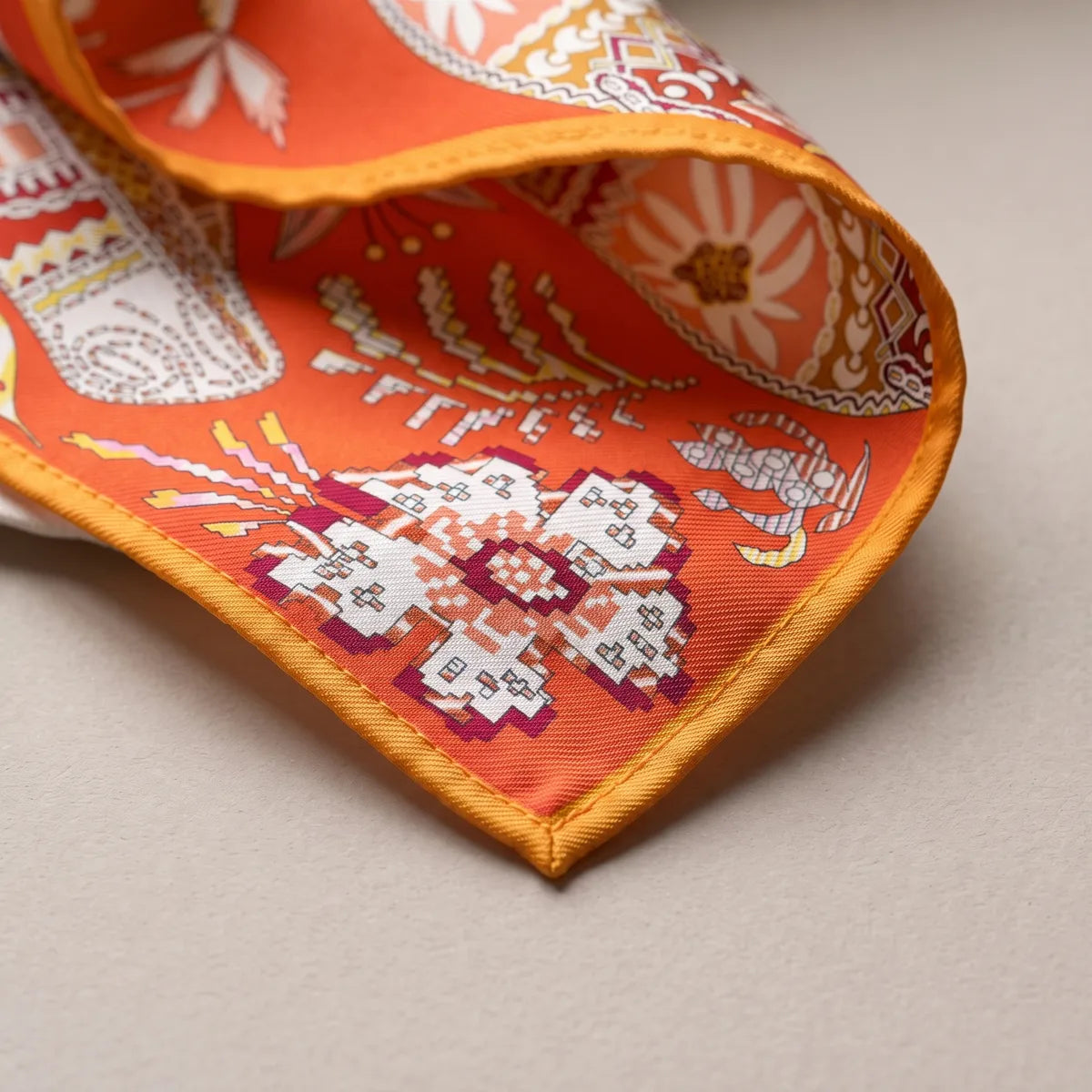 Corner of the orange floral shawl: a pixel-like crimson flower on orange and the narrow saffron hem