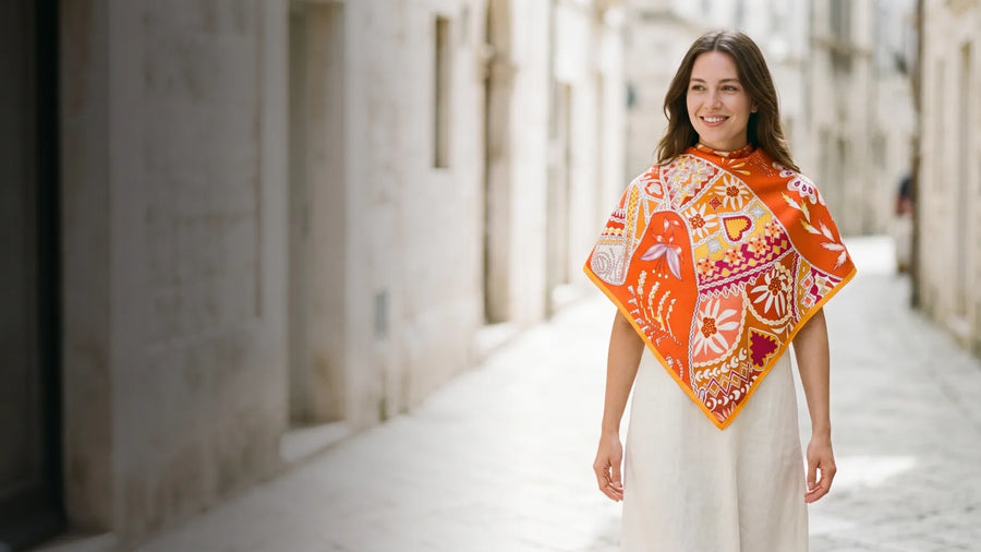 Smiling woman wearing an orange patchwork floral silk shawl over her shoulders in a sunlit street