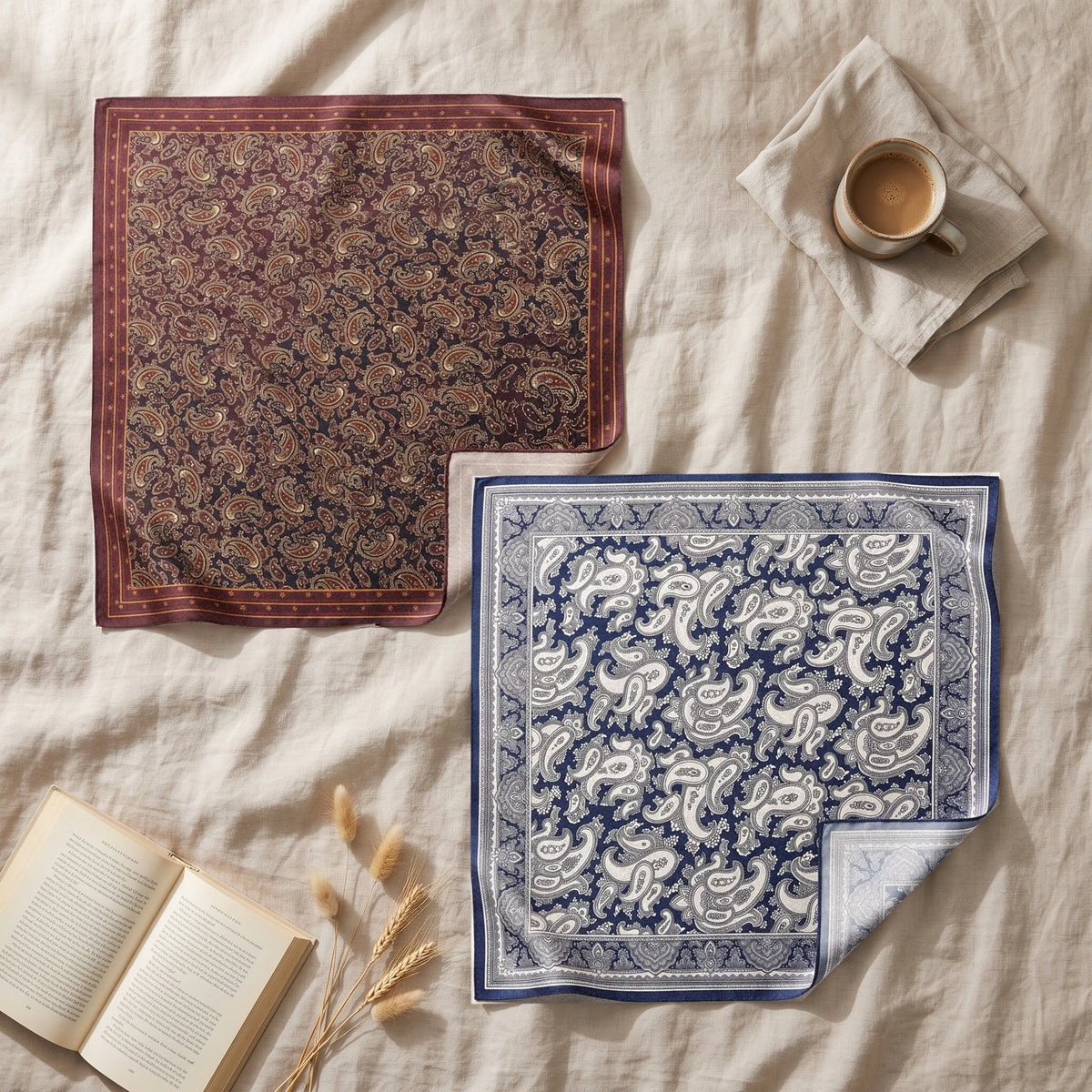 Burgundy and navy paisley bandanas overlapping on linen with a cup of coffee and dried grasses