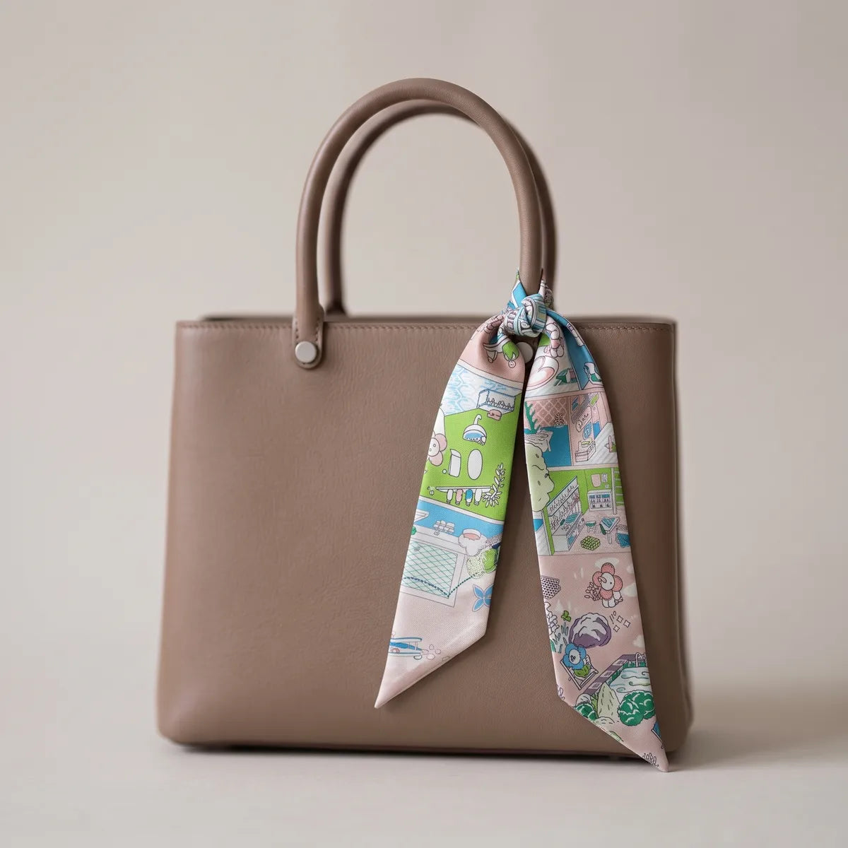 Pastel pink house print skinny silk scarf tied on a taupe leather bag handle