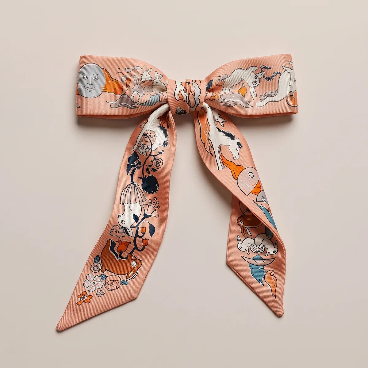 Peach skinny silk scarf tied in a flat bow, a moon face on one loop and a galloping white horse on the other