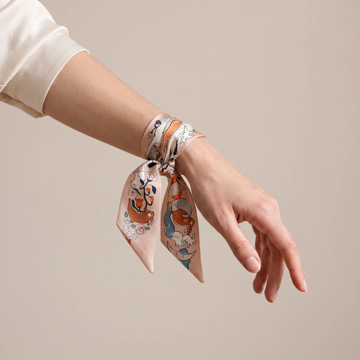 Peach skinny silk scarf wrapped around the wrist and tied, the two ends hanging below