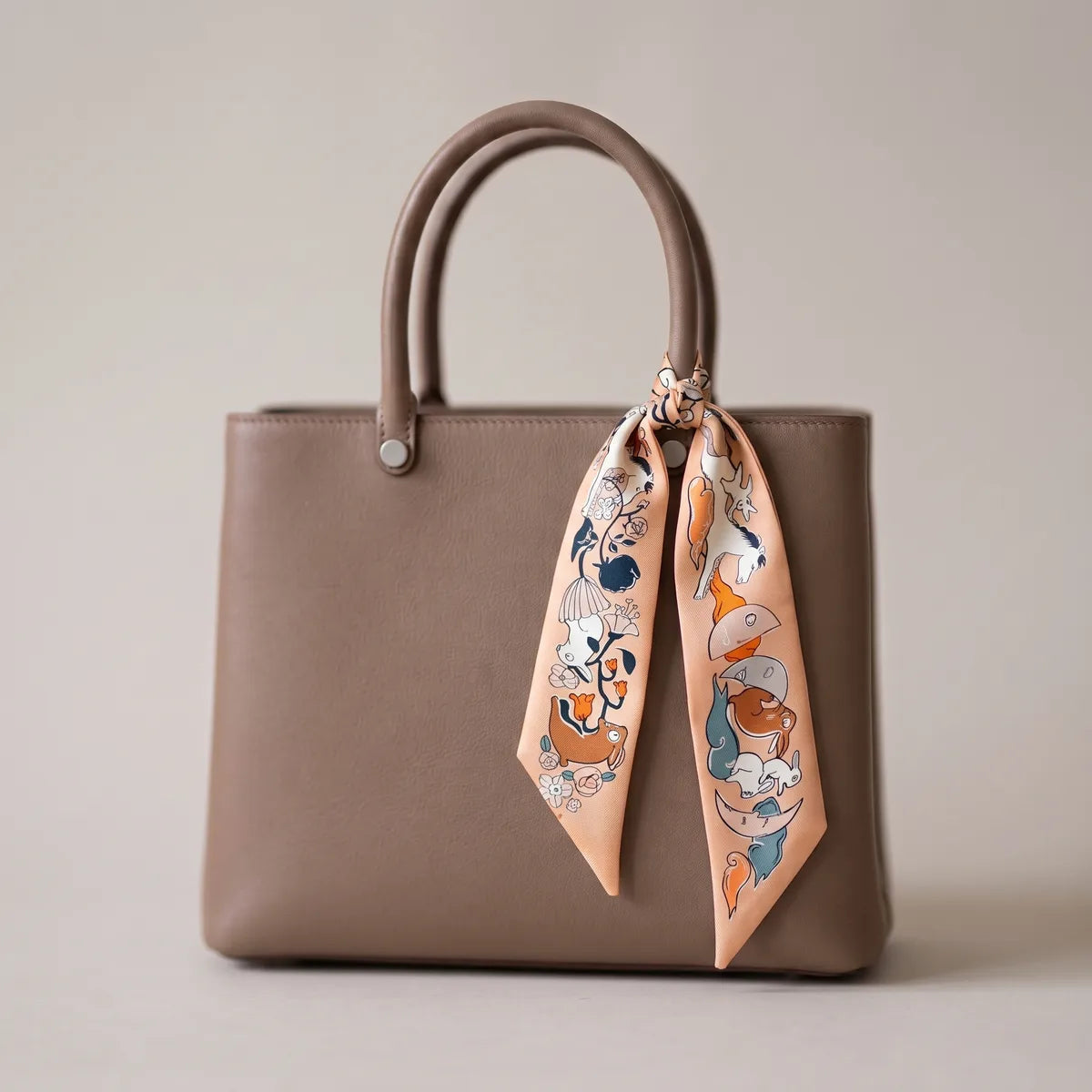 Peach moon print skinny silk scarf tied to the handle of a taupe leather bag