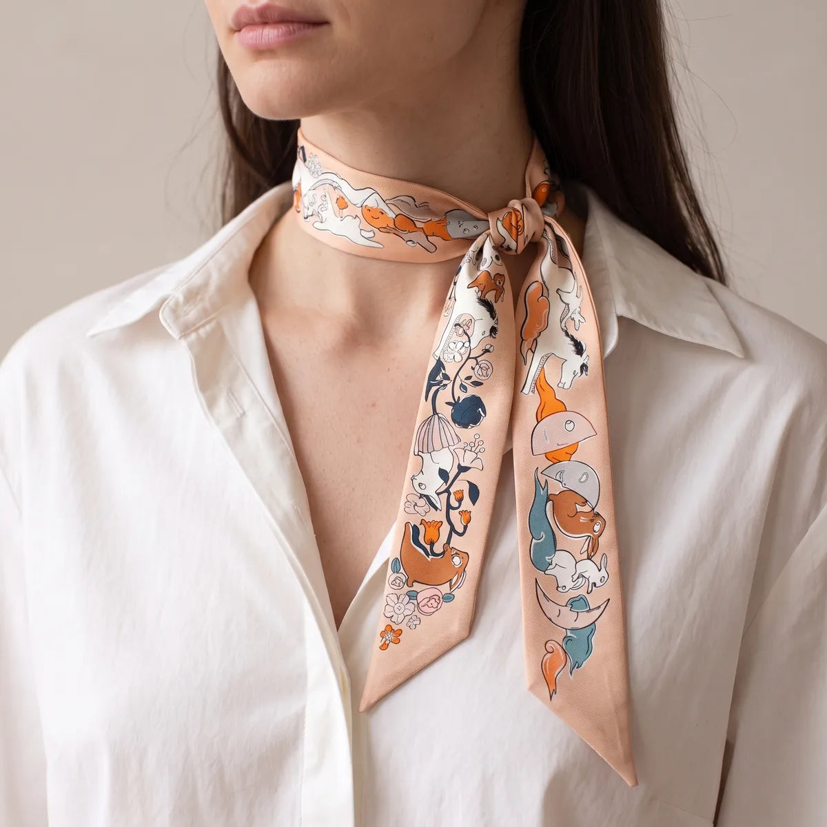 Peach moon print skinny scarf knotted to one side of the neck over a white shirt collar