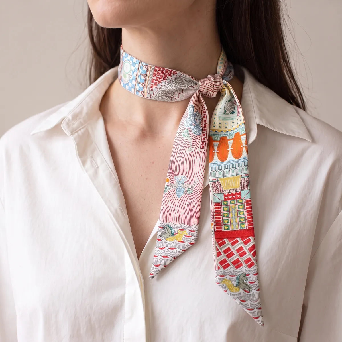 Pink architecture skinny scarf knotted at the side of the neck over a white shirt, ends at different lengths