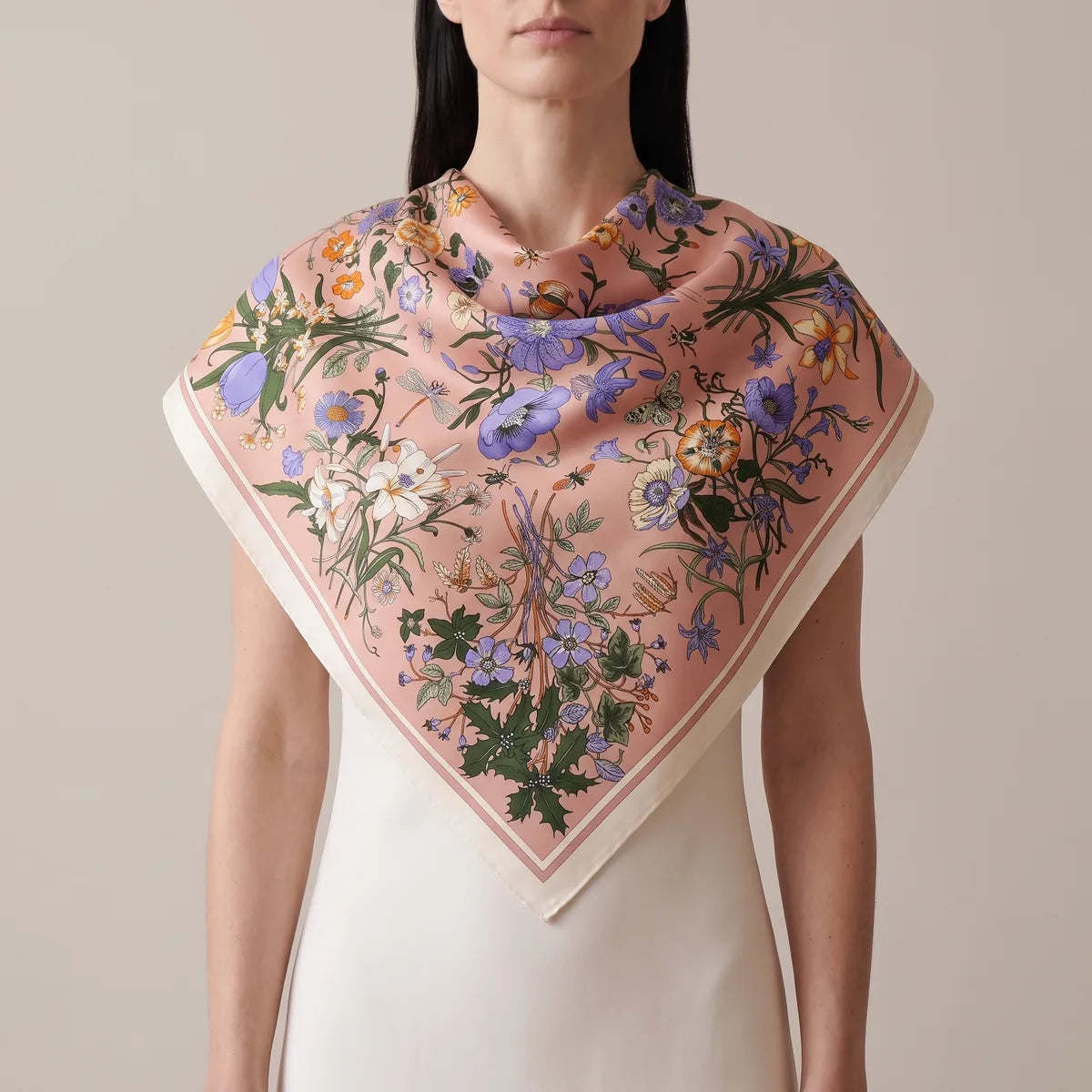 Woman in a cream dress wearing the pink botanical shawl over her shoulders, flowers at the point