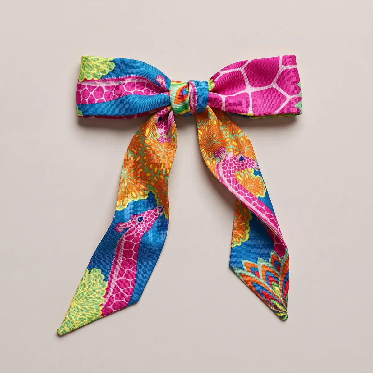 Fuchsia and azure skinny silk scarf tied into a flat bow, a pink giraffe running down one loop
