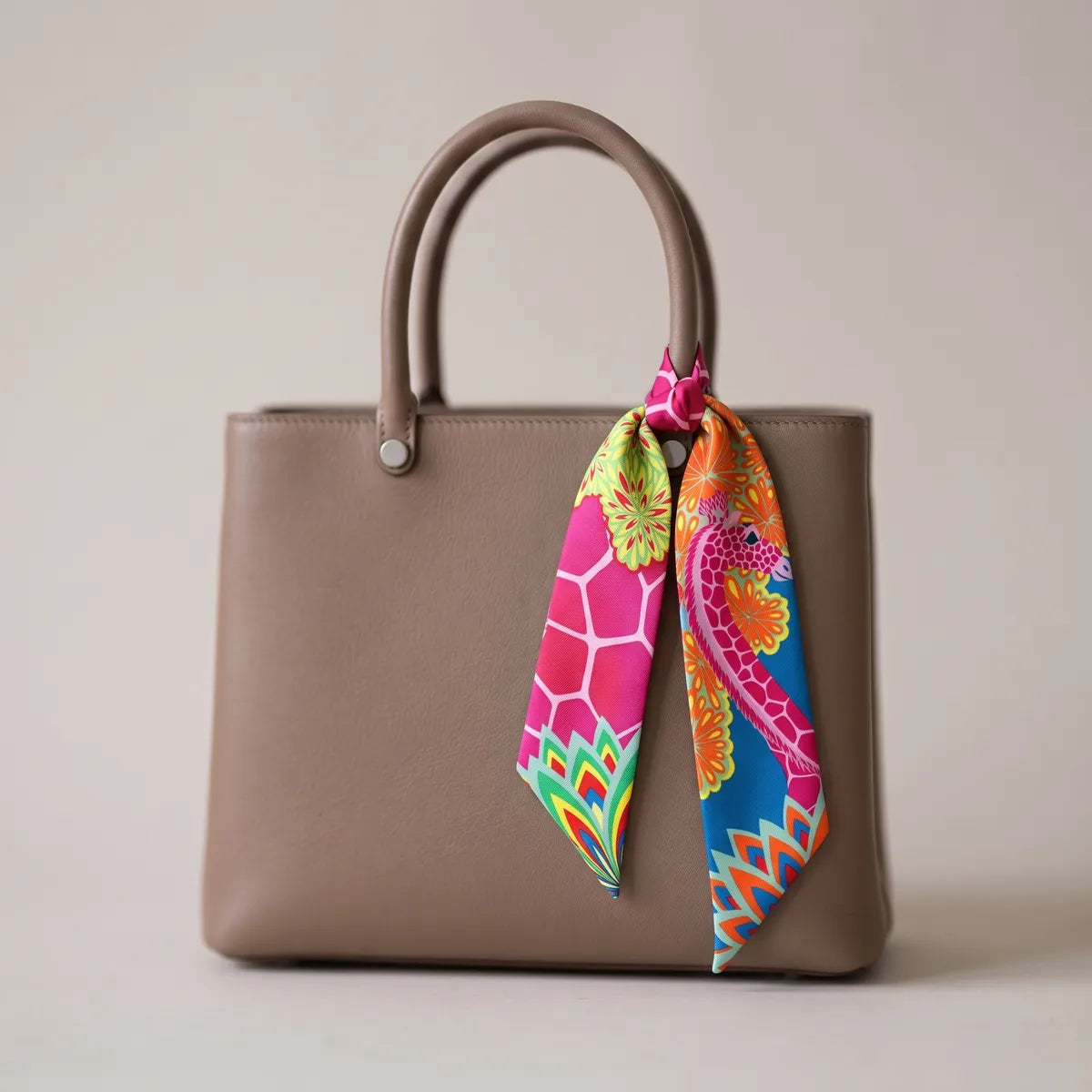 Fuchsia giraffe print skinny silk scarf knotted on the handle of a taupe leather bag