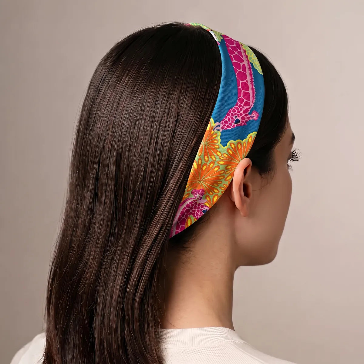 Pink giraffe print skinny scarf worn as a headband over long dark hair, seen from behind