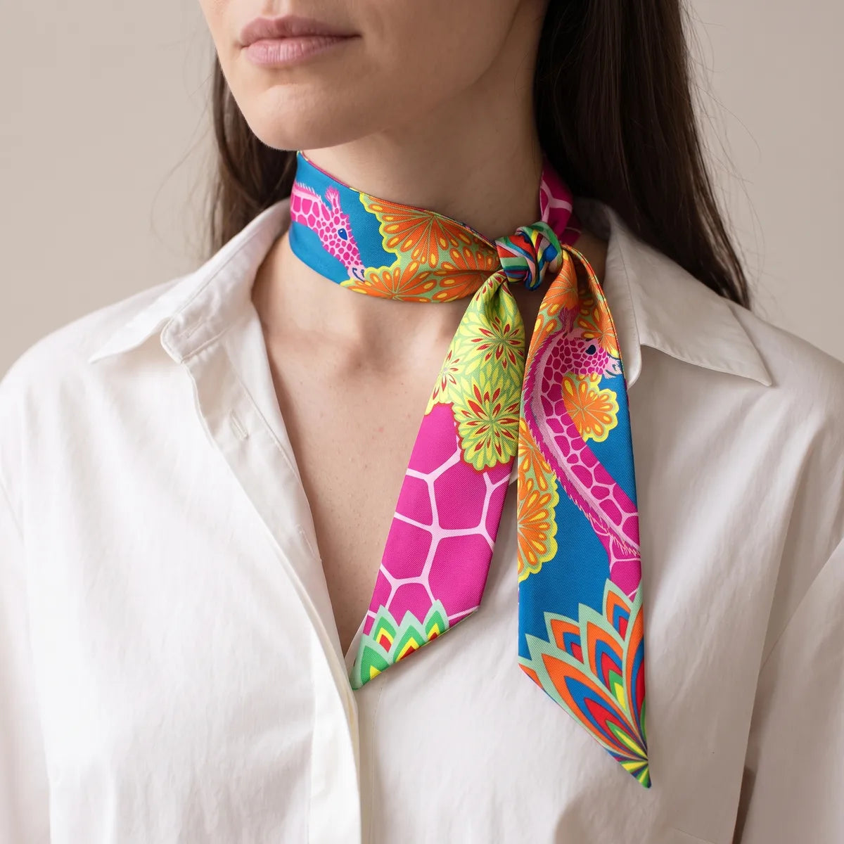 Woman in a white shirt wearing the pink giraffe skinny scarf knotted at one side of her neck