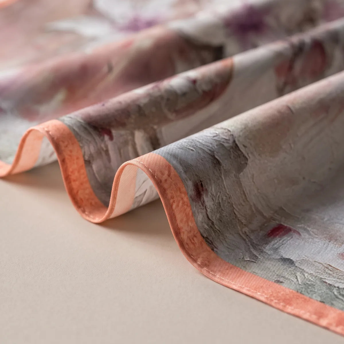 Coral edge of a pink floral silk scarf curling through loose folds of gray and rose brushwork