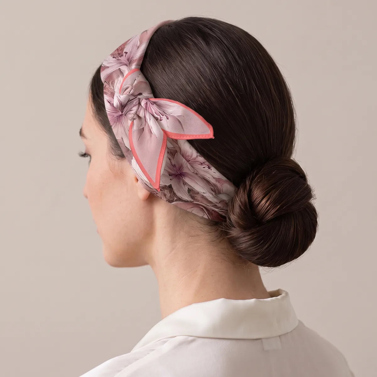 Pink floral silk bandana folded into a band around the head, the knot above the ear, a low bun at the back