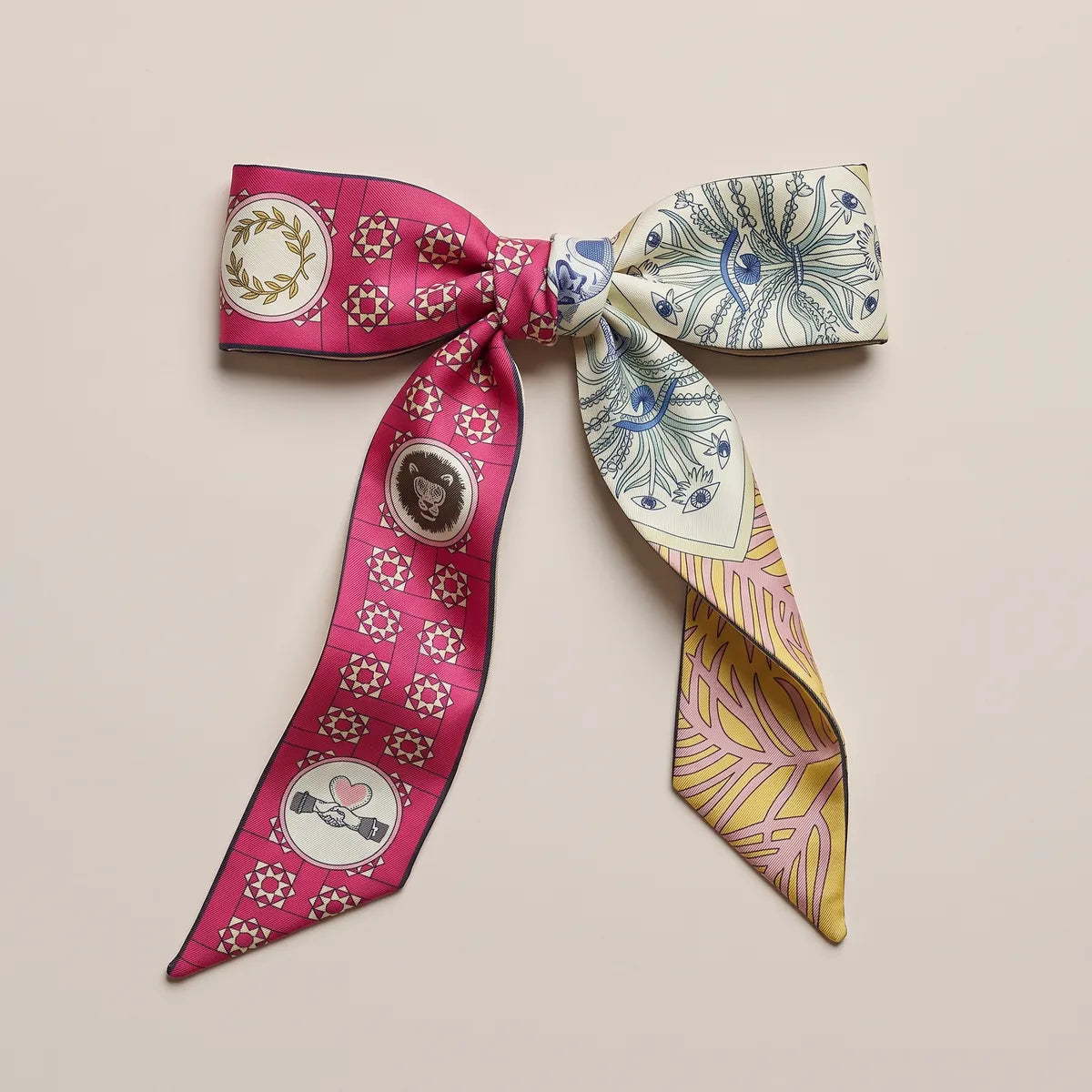 Raspberry and cream skinny silk scarf tied in a bow, laurel wreath on one loop and blue ornament on the other