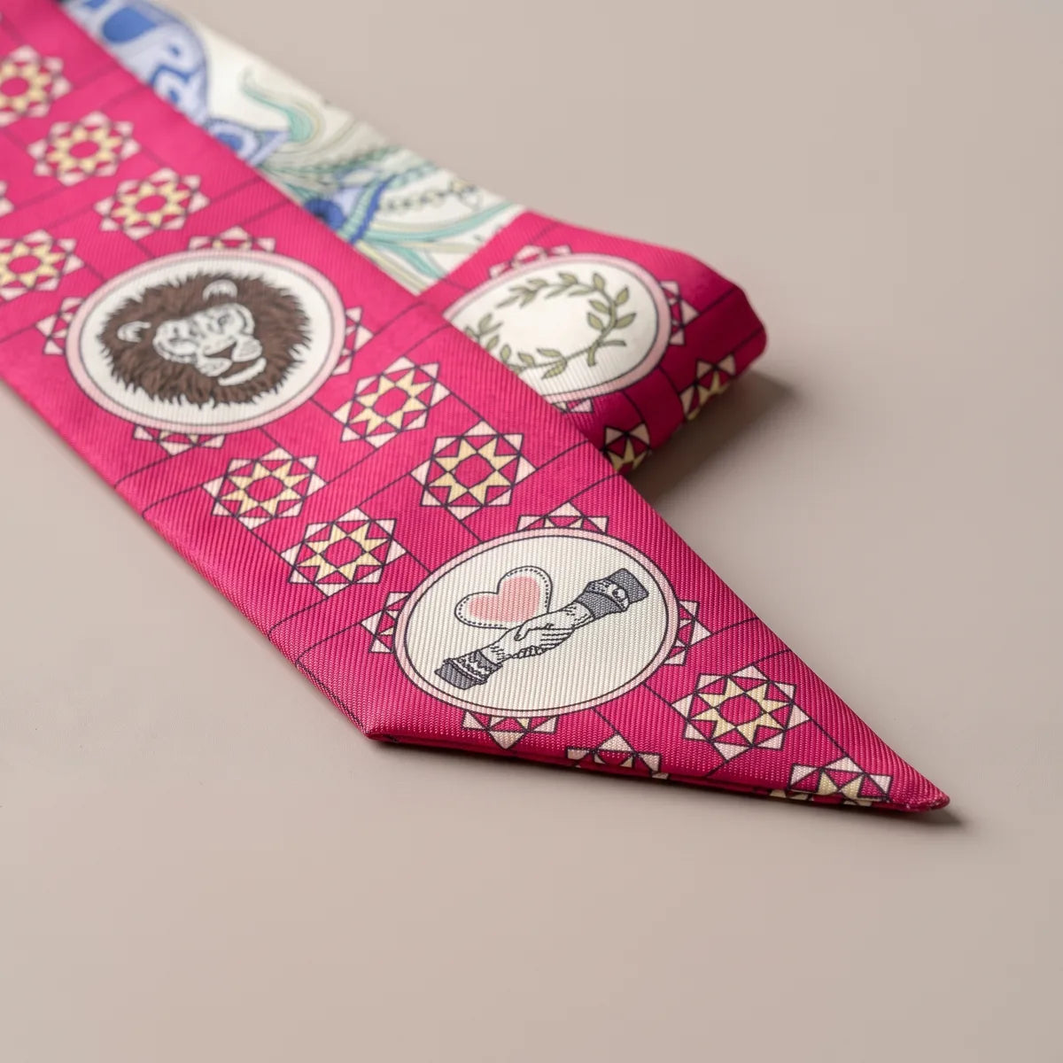 Folded tip of the pink skinny scarf: lion head and clasped hands medallions on star tiles