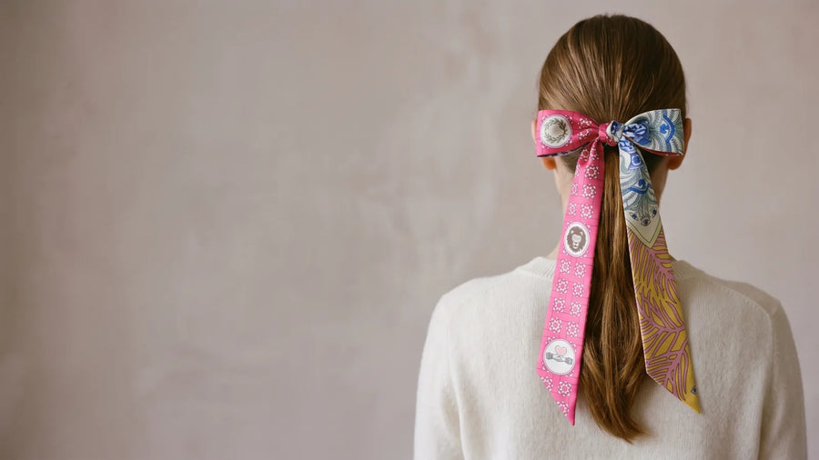 Pink skinny silk scarf tied in a bow around a ponytail, seen from behind