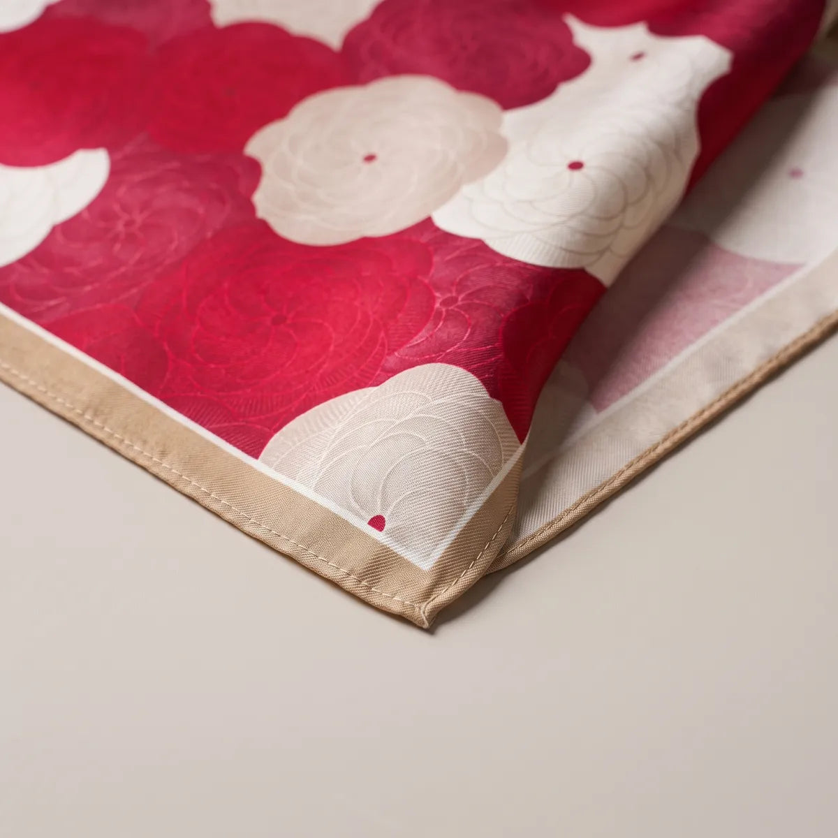 Corner of the red floral bandana: a cream bloom with a red dot, tone-on-tone crimson flowers and the tan hem