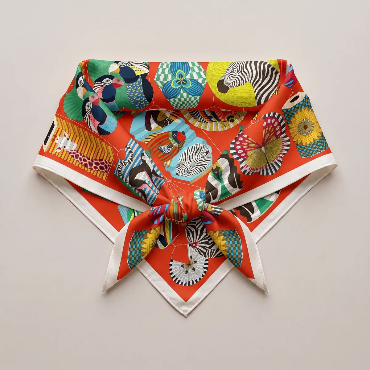 Red silk square knotted into a triangle and laid flat, a zebra lantern near the top and cream edges