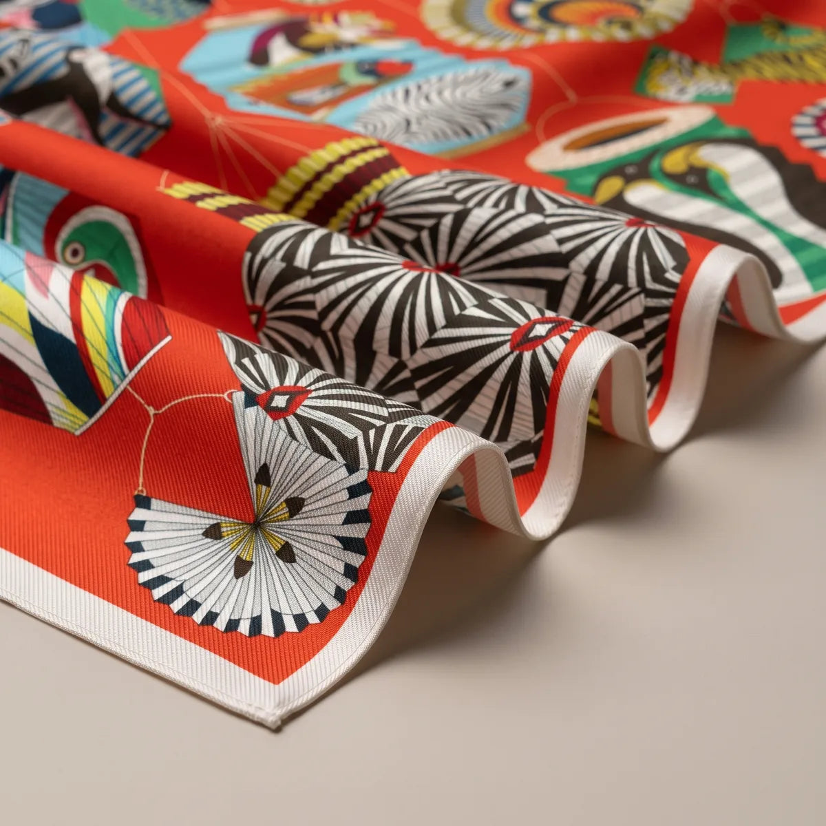 Close-up folds of the vermilion scarf: a black and white starburst lantern and a black and white fan