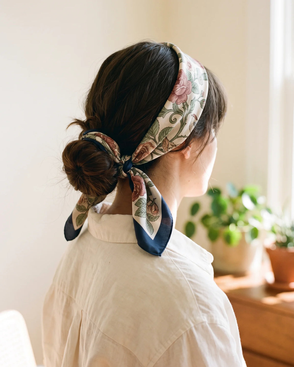 Woman with a floral silk bandana tied in her hair over a low bun, seen from behind
