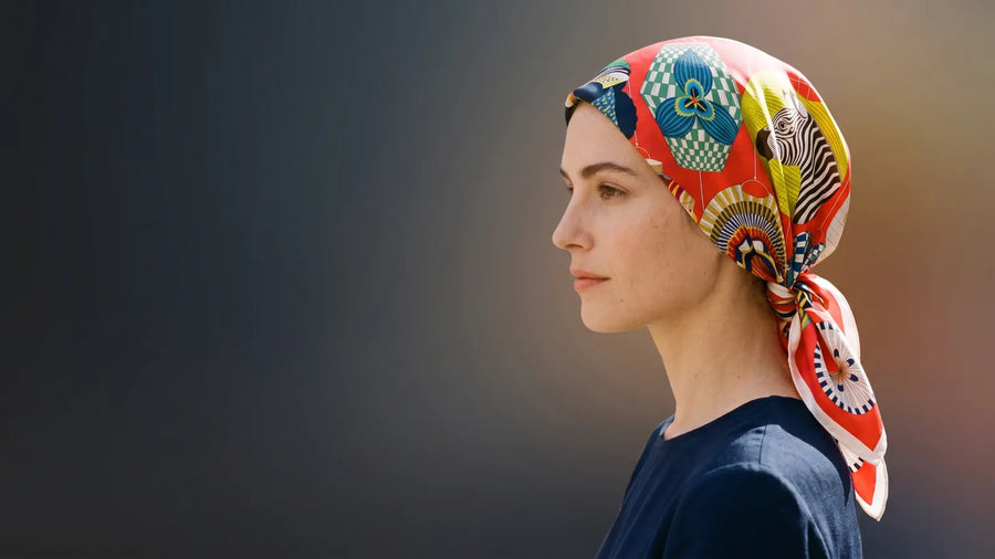 Woman in profile wearing a red lantern print silk square as a head wrap knotted at the nape