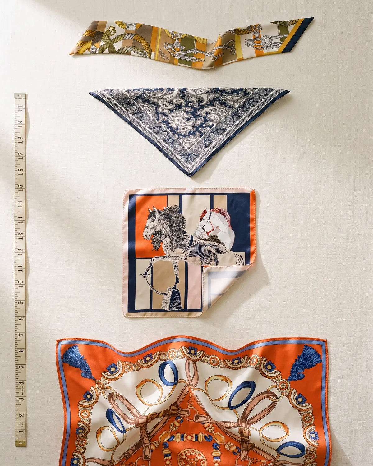 Silk scarf sizes from smallest to largest: skinny scarf, bandana, small square and shawl, next to a tape measure in inches