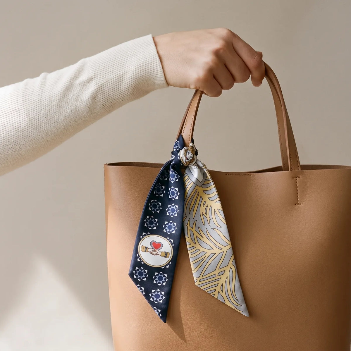 Navy medallion print skinny silk scarf with long tails on a tan leather tote handle