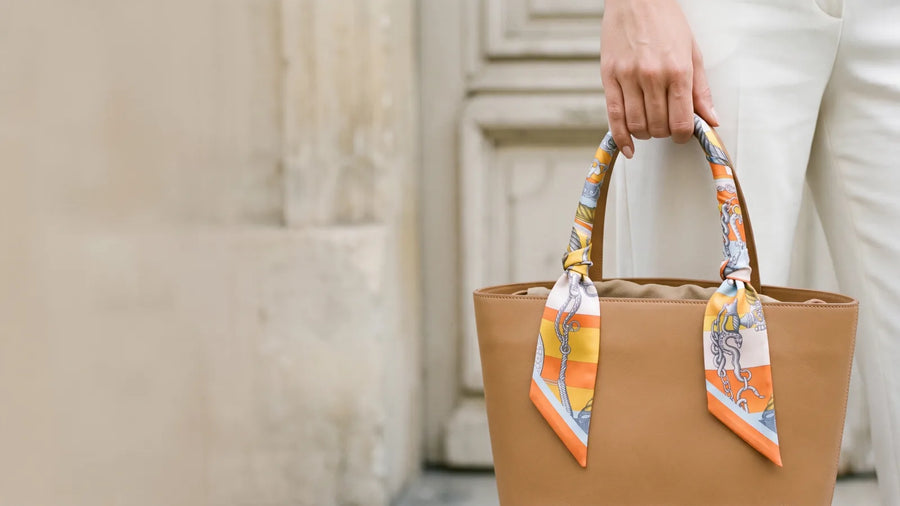 Orange chain print skinny silk scarf wrapped and knotted on a tan leather bag handle