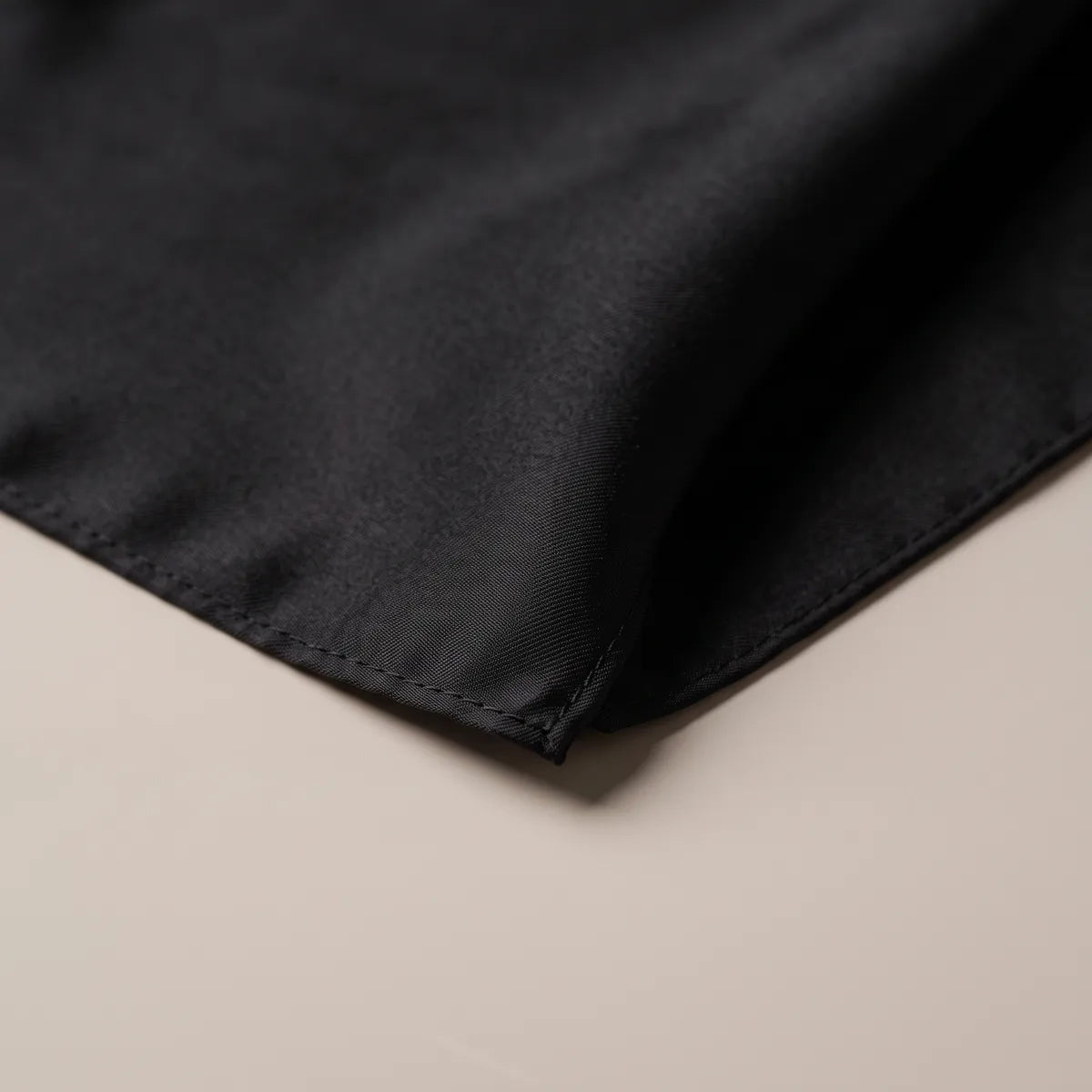 Close view of a stitched black hem at the corner of the plain silk bandana
