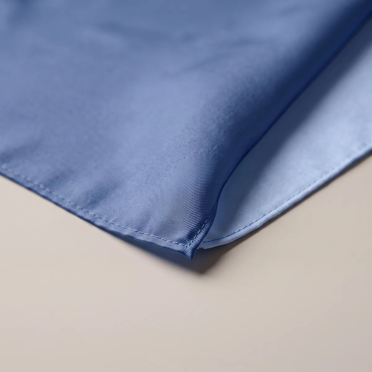 Stitched corner of the solid blue bandana, showing the fine hem and the sheen of the silk