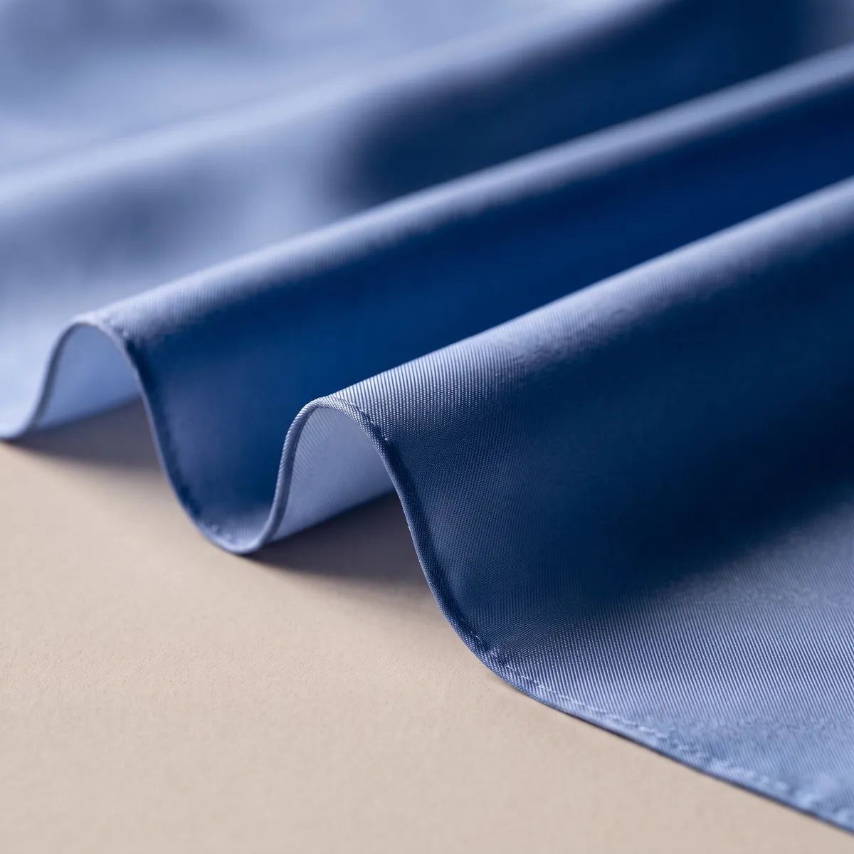 Close-up of periwinkle blue silk falling in soft waves, the narrow hem along the edge