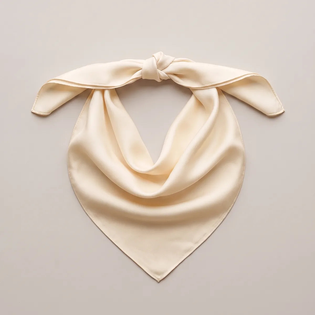 Buttery cream bandana with one knot at the top, laid out so the point curves below