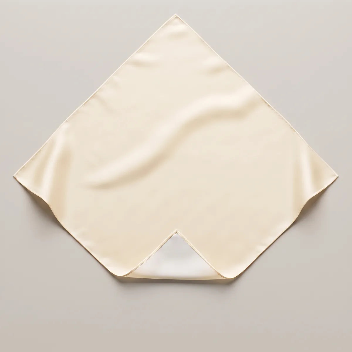 Solid cream silk bandana on a pale surface, point at the top, a turned-back corner showing a whiter reverse