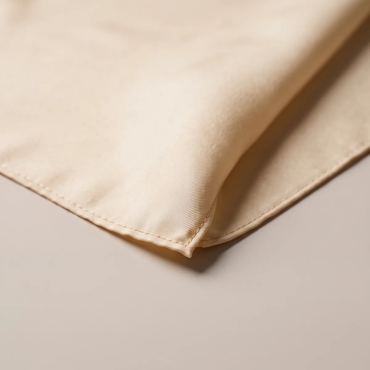 Corner of the solid cream bandana in close-up, the narrow hem folded under