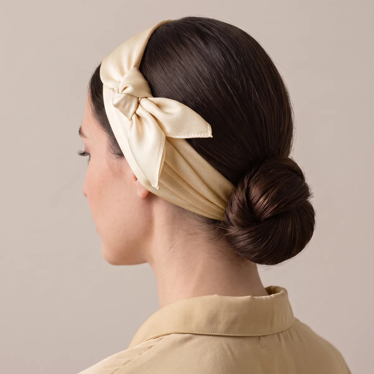 Cream silk scarf worn as a headband over dark hair, knotted above the ear, low bun behind