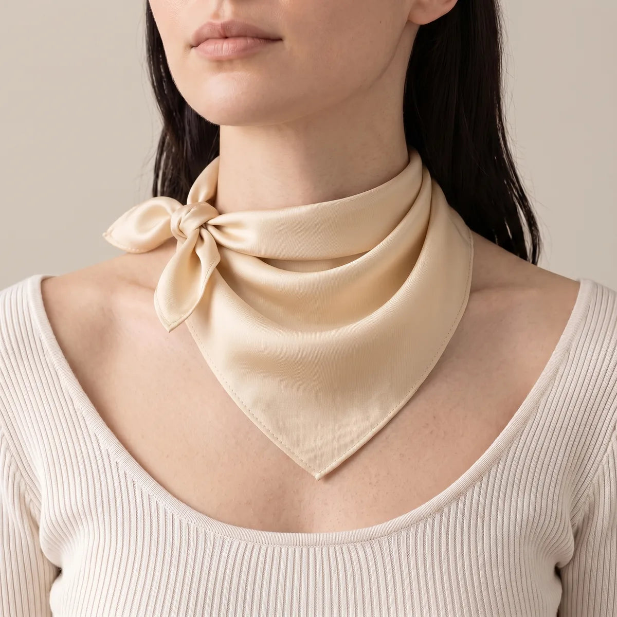Cream silk bandana knotted beside the neck, tips pointing out, over a pale ribbed top