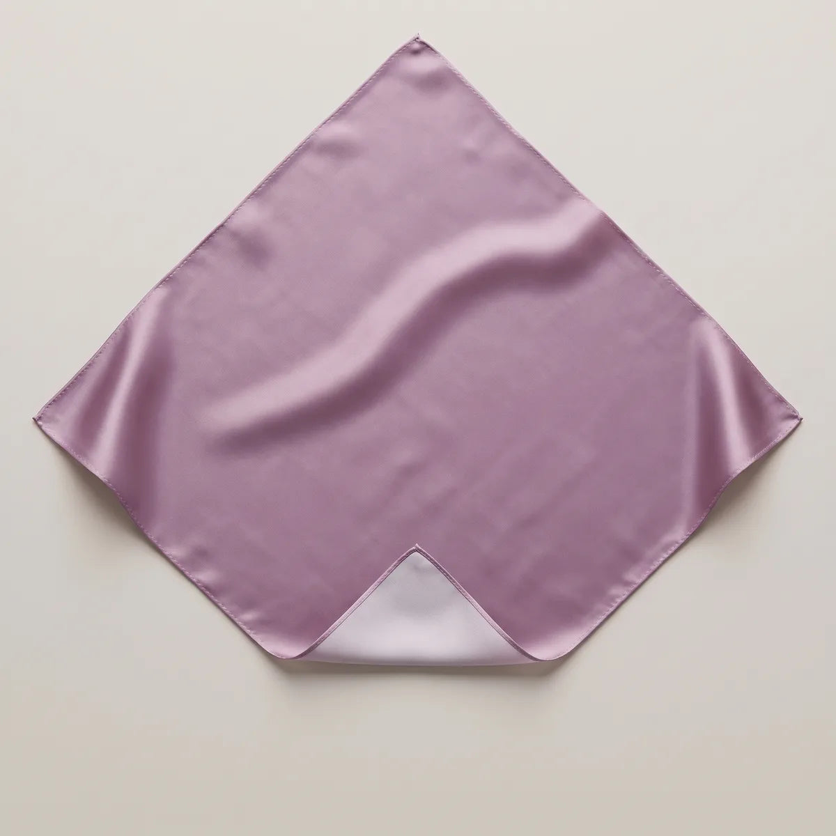 Solid lilac silk bandana flat on a pale surface, its folded corner revealing paler powder lilac